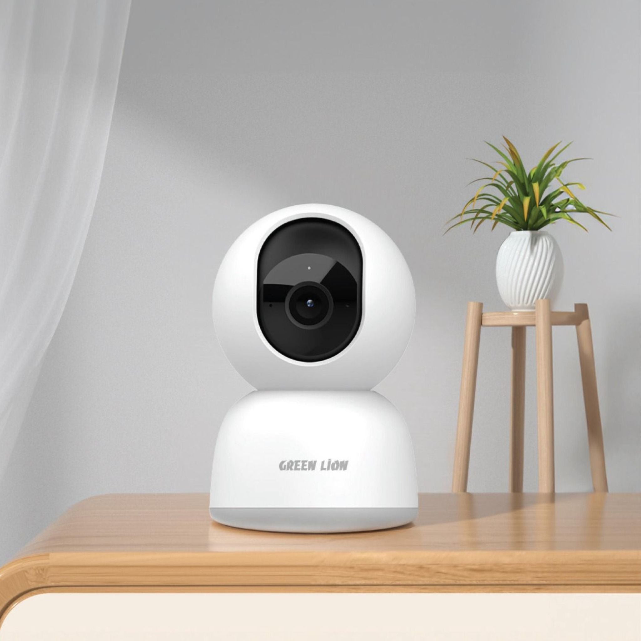 A white dome-style wireless surveillance camera with the brand name 'Green Lion' on the base, placed on a wooden table in a home environment.